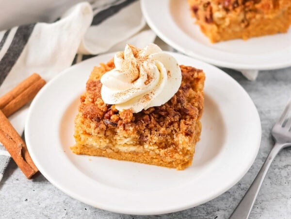 Pumpkin crunch cake slice on white plate with whipped cream on top.