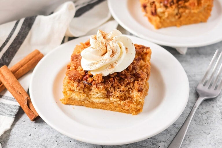 Pumpkin crunch cake slice on white plate with whipped cream on top.