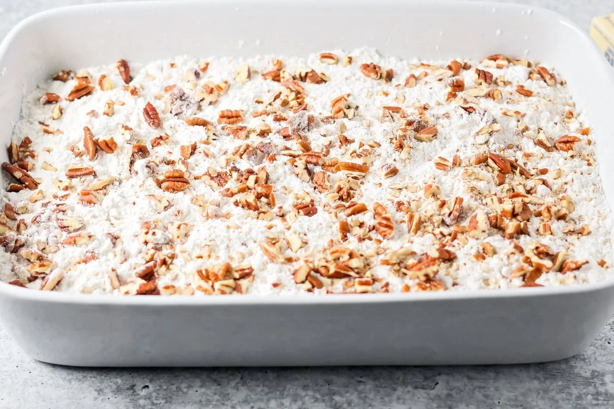 Pecans sprinkled over cake mix layer of pumpkin cake.