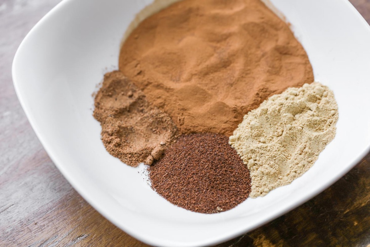 4 spices in a white bowl to blend for pumpkin pie spice.