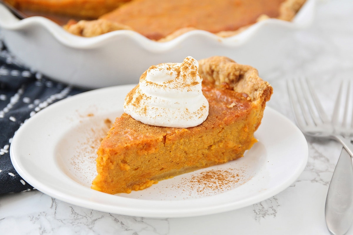 Slice of sweet potato pie on a white plate topped with whipped cream.