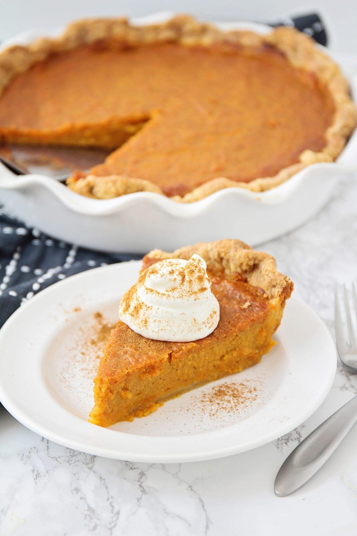 A slice of homemade sweet potato pie recipe with a dollop of whipped cream served on a white plate.