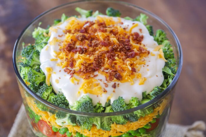 Deliciously customizable 7 Layer Salad is filled with just the right amount of goodness. It's perfect to make ahead! 7 layer salad recipe dressed and topped with bacon and cheese.