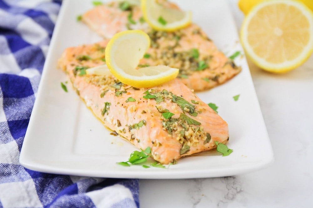 A photo of baked salmon topped with a slice of lemon, served on a white platter.
