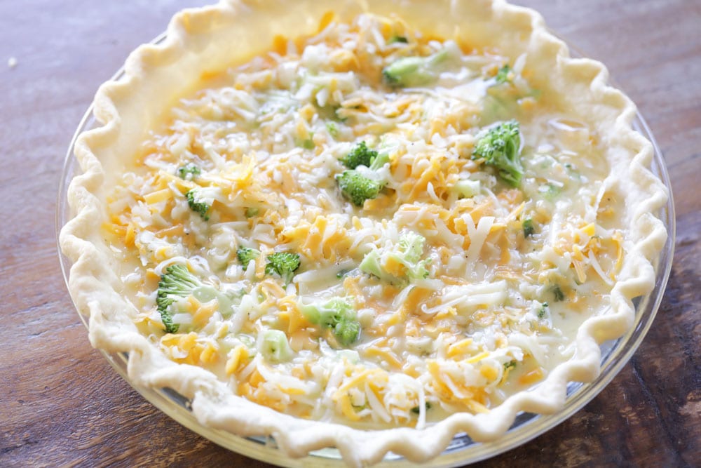 Broccoli, egg, and cheese mixture in a pie crust ready to be baked.
