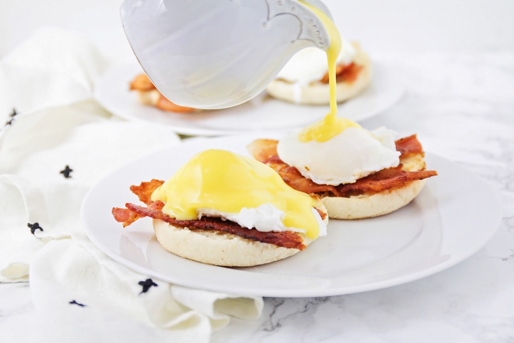 Pouring hollandaise sauce over eggs Benedict