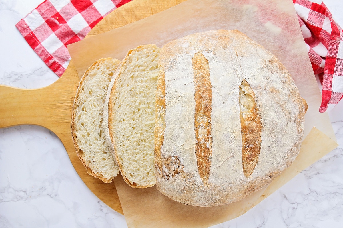 A round loaf of No Knead Bread on a piece of parchment paper on a wooden pizza peel. 