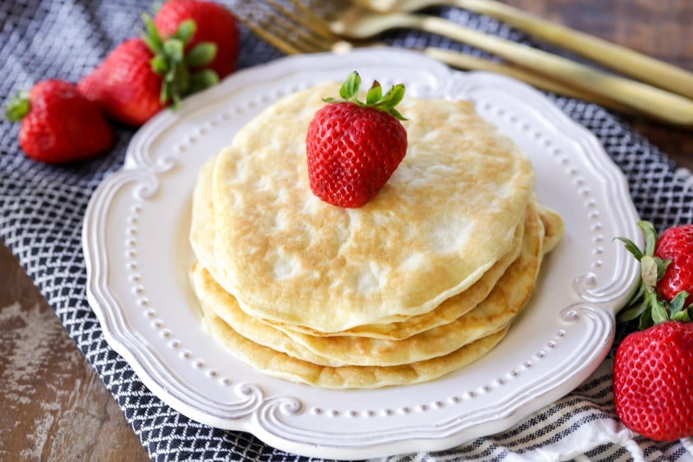 A stack of protein pancakes with a strawberry on top on a white plate.