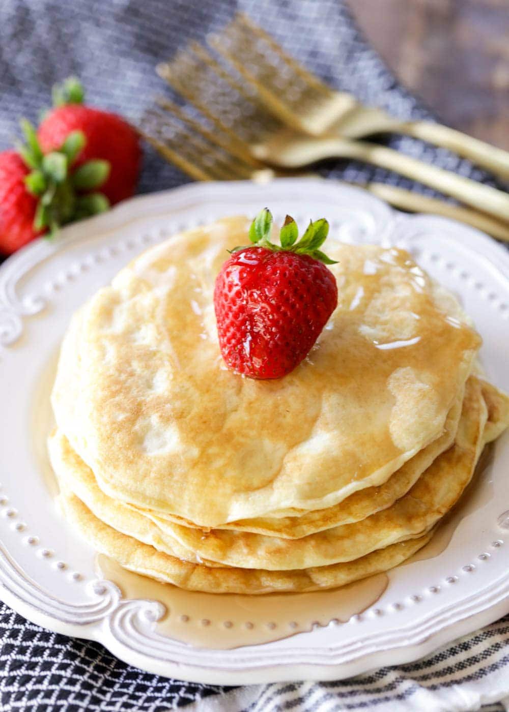 A stack of protein powder pancakes with a strawberry and syrup.