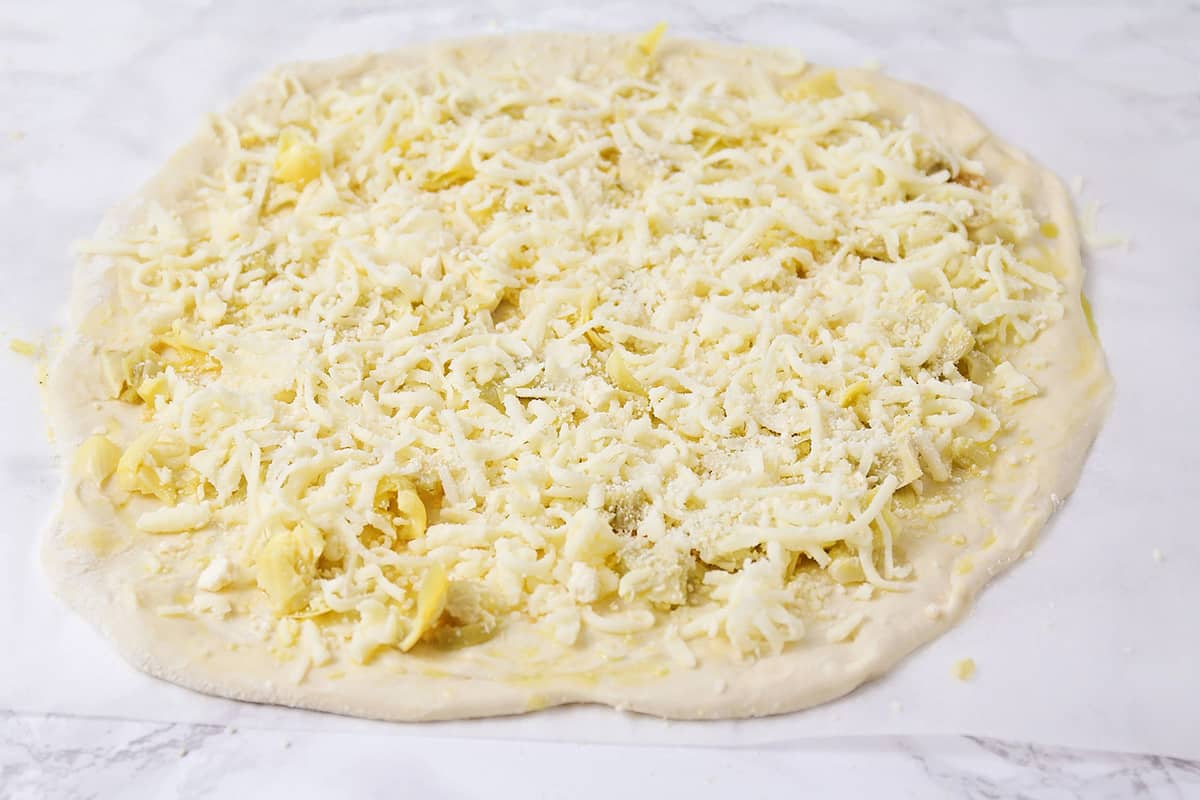 Adding shredded cheese to the top of pizza crust.