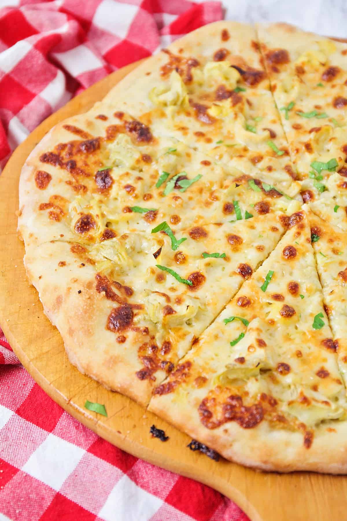 Close up of artichoke pizza sliced and garnished with herbs.