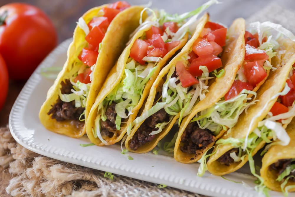 Ground beef tacos filled with lettuce and tomato, served on a plate.