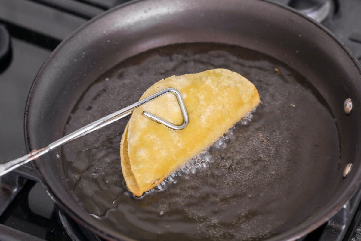 Ground beef tacos being fried up in a pan of oil.