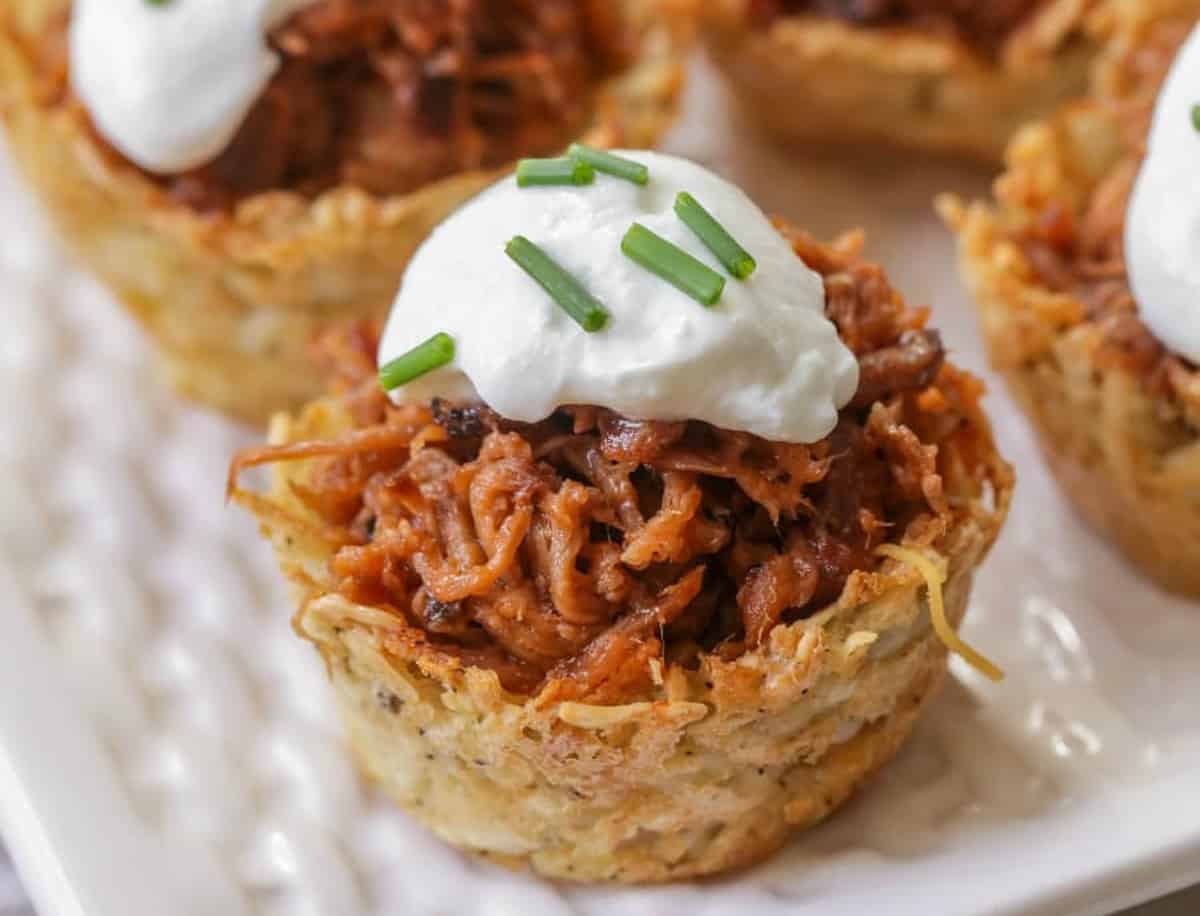 Healthy Appetizers - Loaded pulled pork cups topped with sour cream and chives on a white plate. 