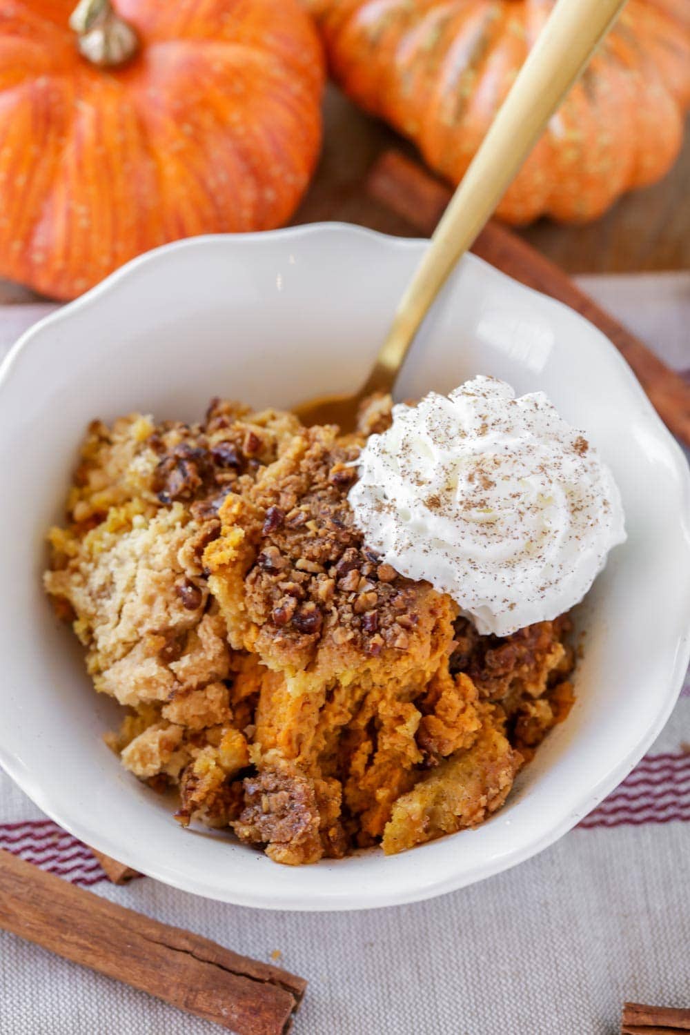 Serving pumpkin cobbler with whipped cream and cinnamon in a white bowl.