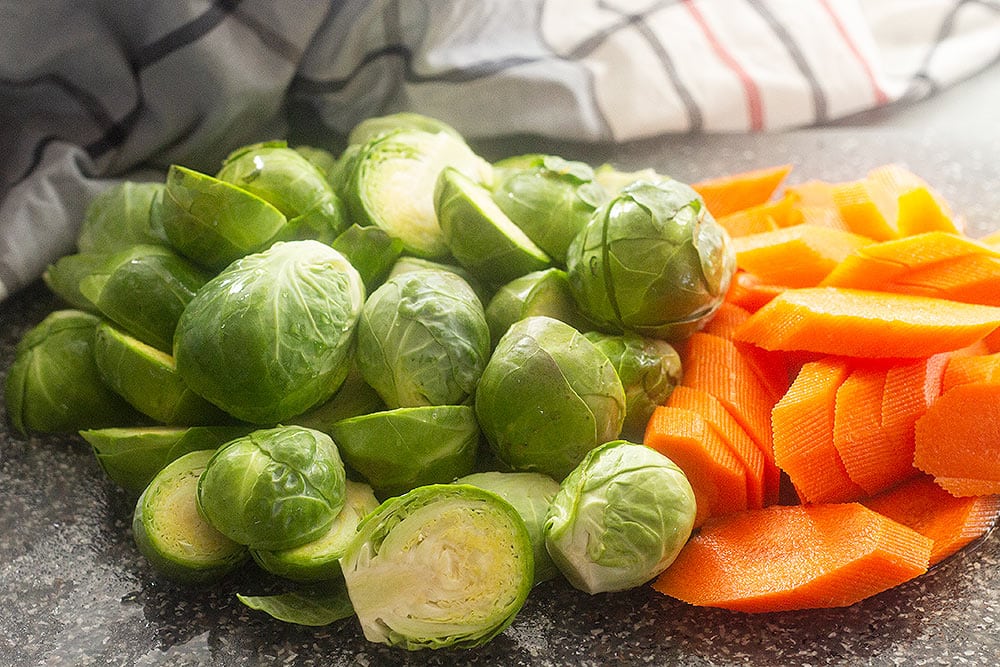 Washed and cut Brussels sprouts and carrots on a counter.