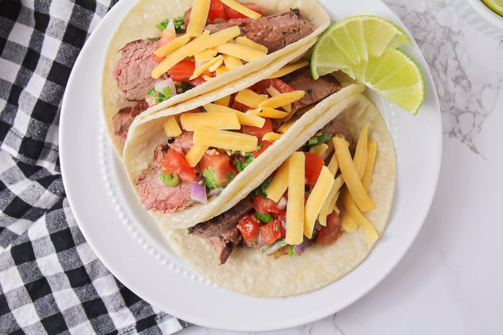 Carne asada tacos on a plate with lime slices