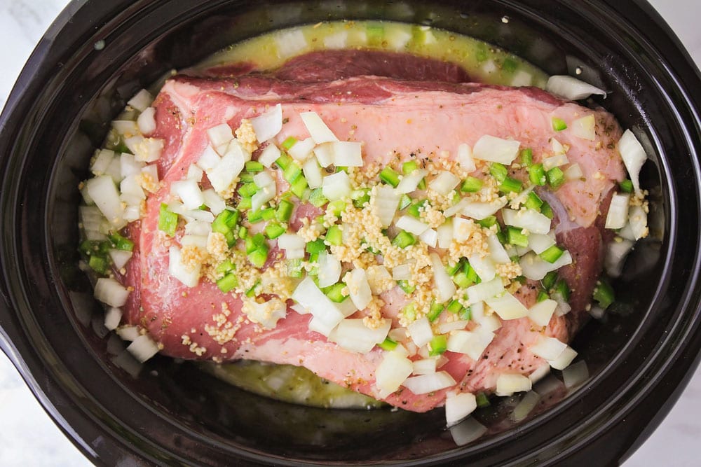 Pork roast inside a slow cooker with onions and seasonings