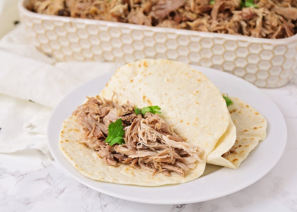 Two carnitas tacos on a white plate topped with cilantro.