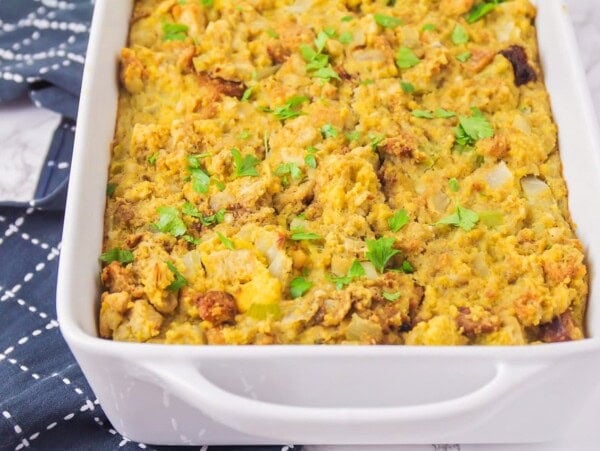 A baking dish of cooked cornbread stuffing topped with fresh herbs.