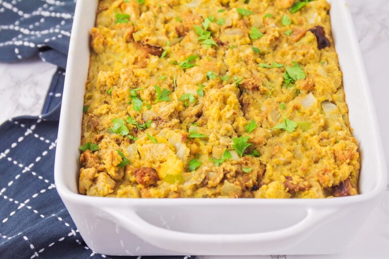 A baking dish of cooked cornbread stuffing topped with fresh herbs.
