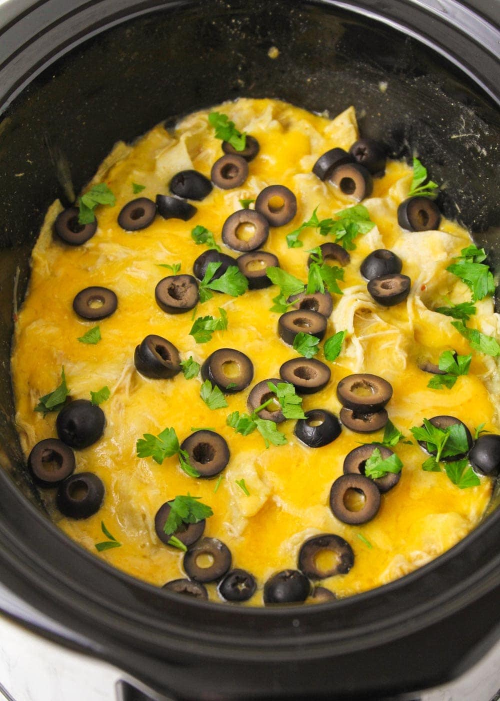 Close up of crock pot chicken enchiladas topped with olives and cilantro.