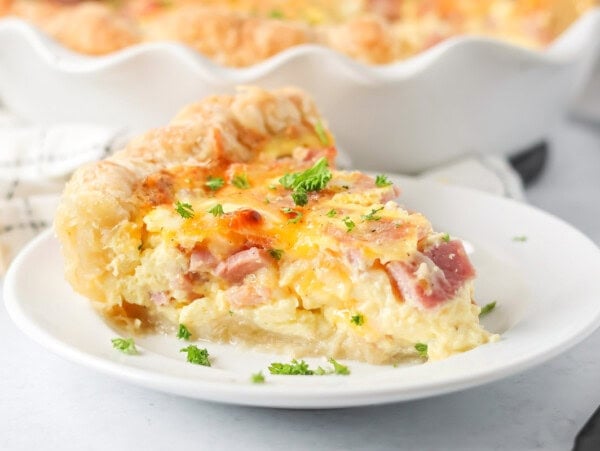 Ham and cheese quiche slice on white plate.