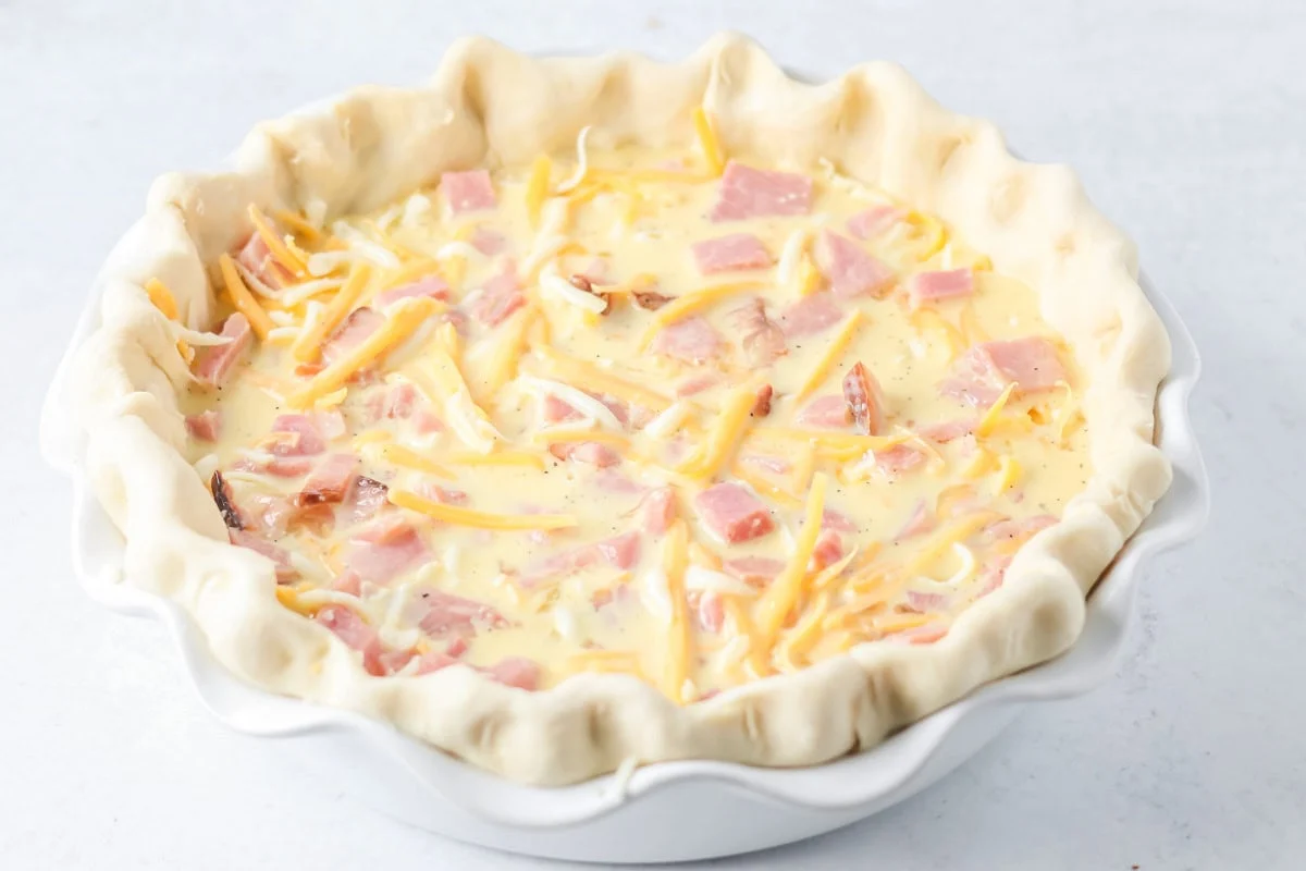 Ham and cheese quiche ingredients in pie dish unbaked.
