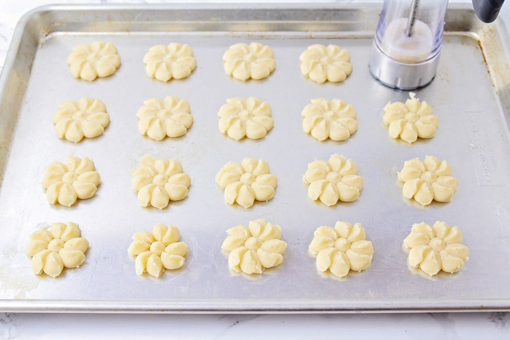 Placing shortbread cookies on a baking sheet with a cookie press