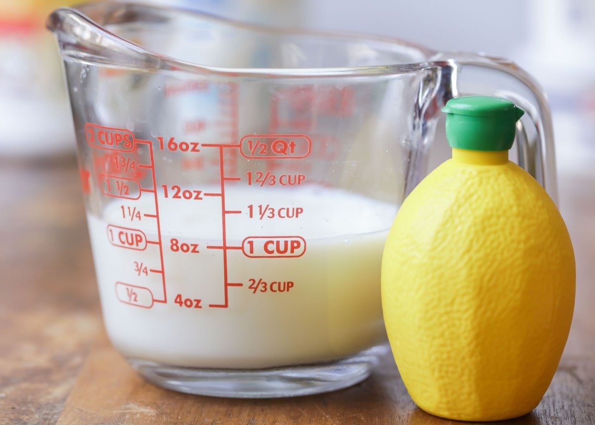 A measuring cup of milk and a container of lemon juice on a counter.