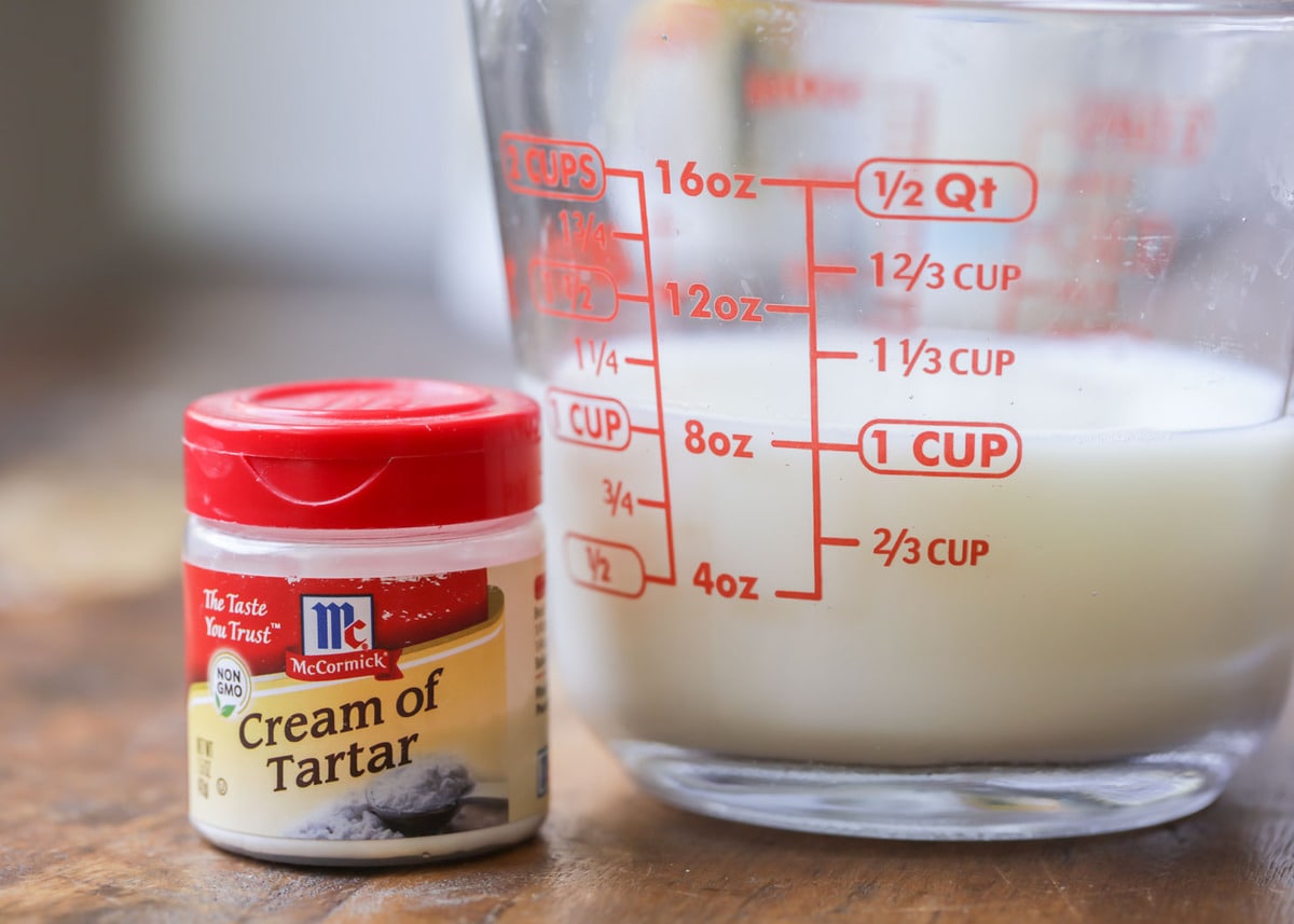 A measuring cup of milk and cream of tartar on a counter.