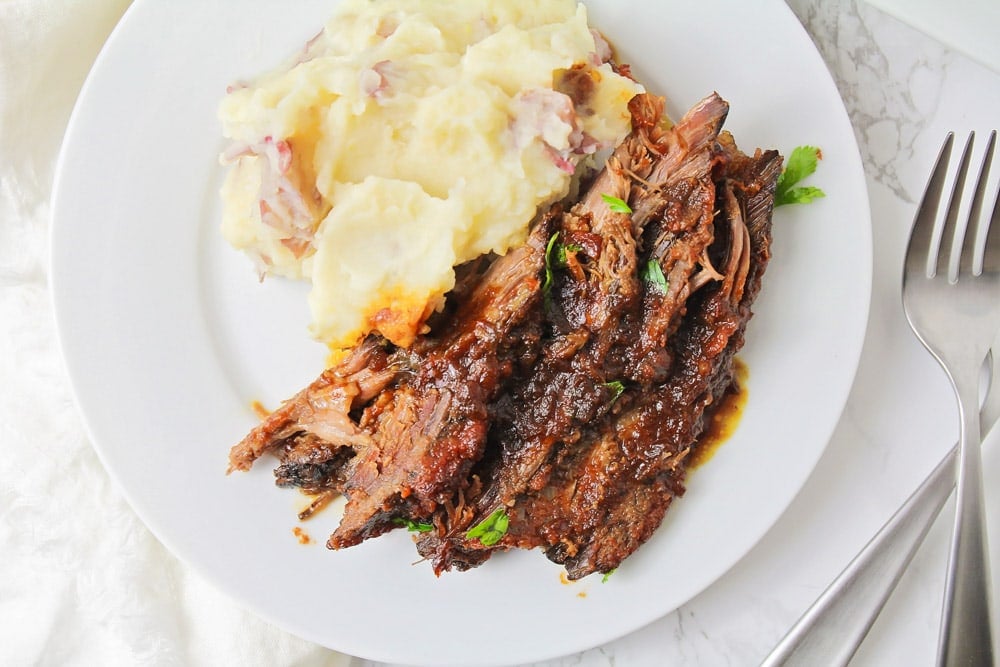 Brisket and mashed potatoes served on a white plate.