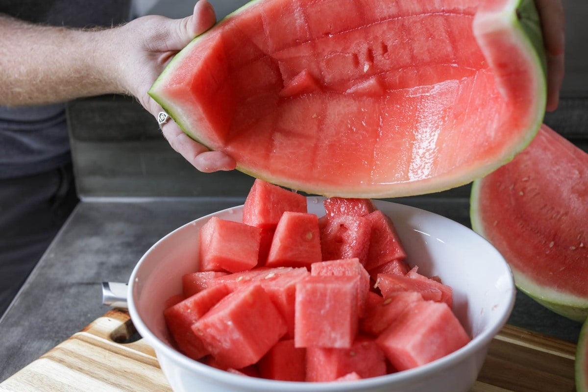 Putting watermelon cubes into a white bowl