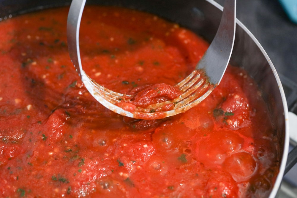 Breaking up tomatoes with pastry cutter as it cooks