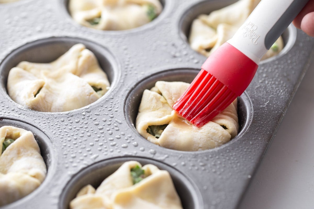 Brushing the top of puff pastry in muffin tin for baking spinach puffs.