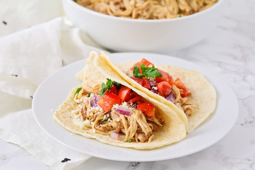 Two pork tacos topped with pico and cheese on a white plate.