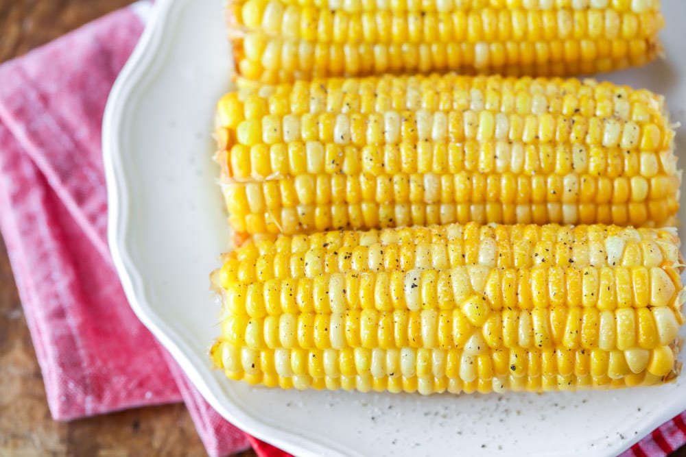 Three cobs of boiled corn on a white plate