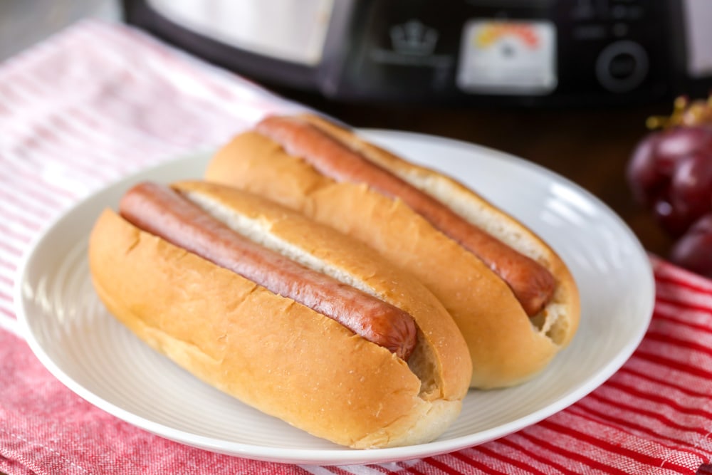 Two hot dogs in buns served on a white plate.