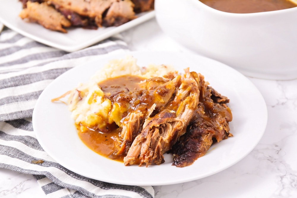 Crock pot pork roast on a white plate with a side of potatoes