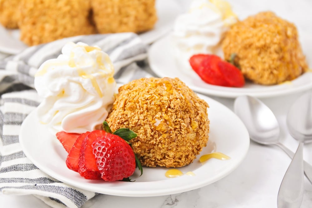 Fried ice cream on a white plate garnished with whipped cream and a sliced strawberry. 