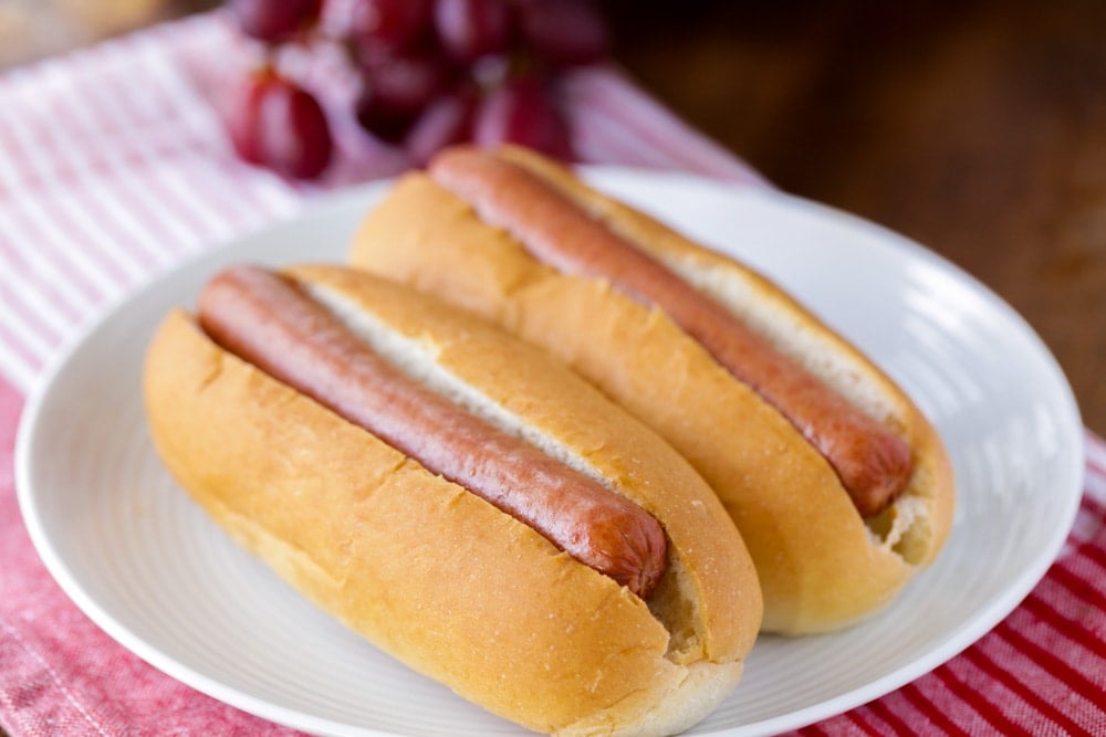 Two boiled hot dogs inside buns on a white plate.