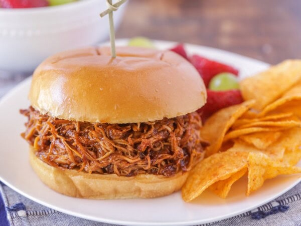 Slow cooker pulled chicken in a sandwich served alongside chips.