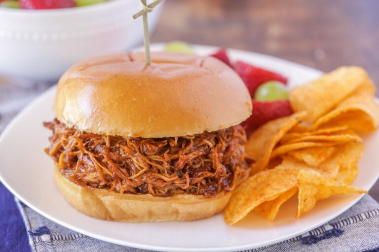Slow cooker pulled chicken in a sandwich served alongside chips.