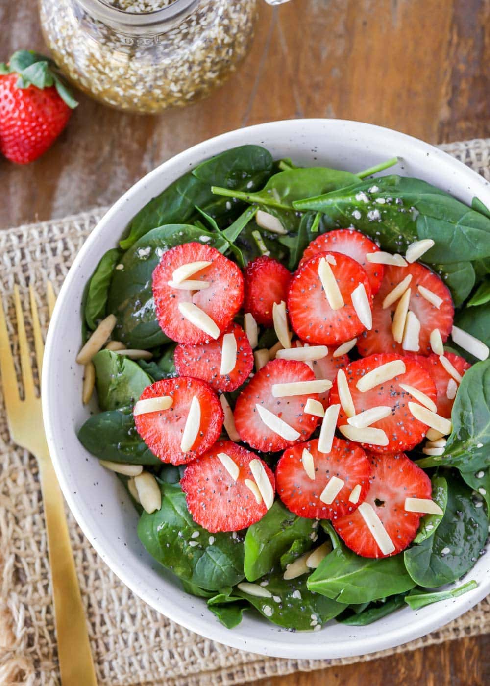 Spinach and strawberry salad topped with nuts in a white bowl