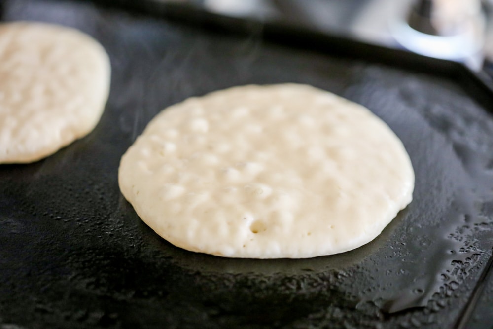 Snowman pancakes cooking on a griddle.