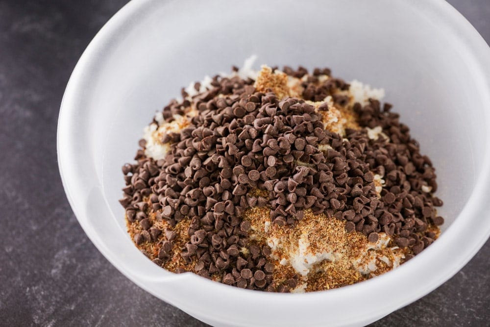 Oats, chocolate chips, and other ingredients mixed in a white bowl.