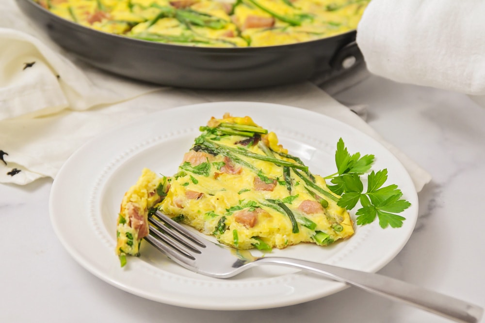 A slice of breakfast frittata filled with ham and asparagus.