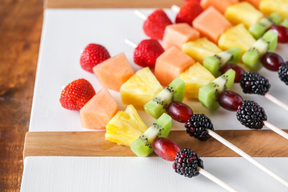 Fruit kabobs consisting of strawberries, cantaloupe, pineapple, kiwi, red grapes and blackberries on wooden skewers. 