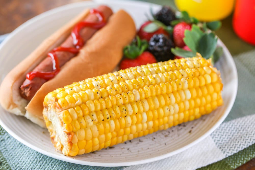 Vegetable side dishes - microwave corn on the cob served with a hotdog and fruit.
