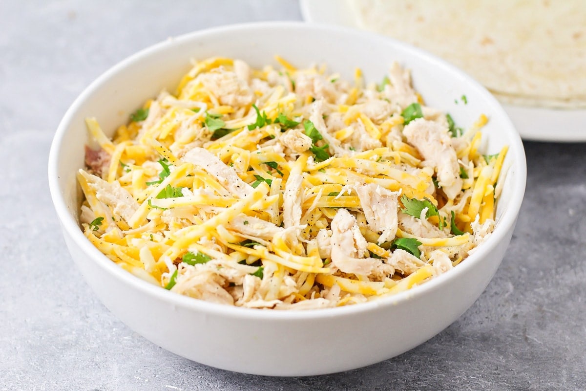 A white bowl filled with shredded chicken, cheese, and seasonings.